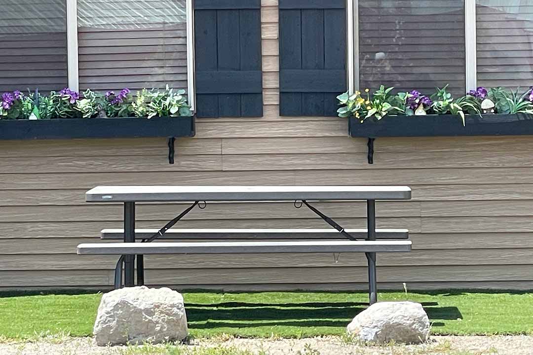 Picnic table outside a cabin with flower-filled window boxes and rustic wood siding